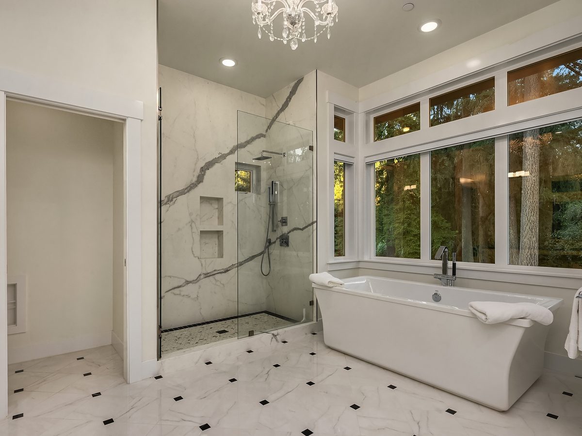 Primary bath with slab-wall walk-in shower, freestanding tub, and a wall of windows onto the forest